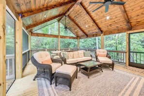 A covered outdoor deck with wicker furniture, a ceiling fan, and a view of the forest. - Sapphire Home w/ Fireplace Near Skiing & Hiking! (Cashiers)