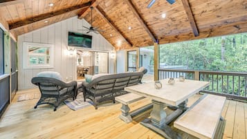 Una terraza de madera con muebles de mimbre y una mesa, con vistas a un área boscosa.