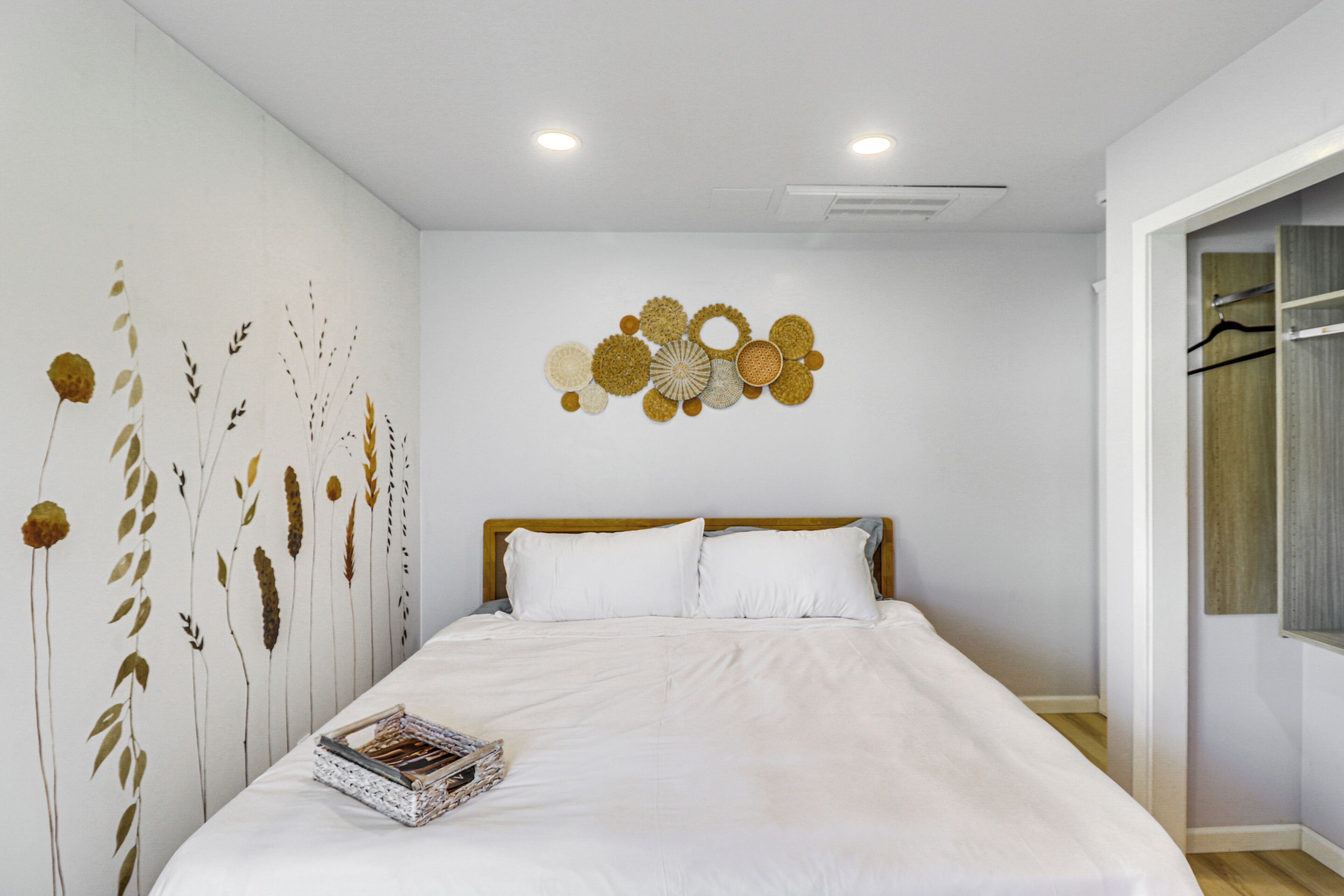 A bedroom with a large bed, white bedding, a wall-mounted artwork of flowers, and a wooden headboard.