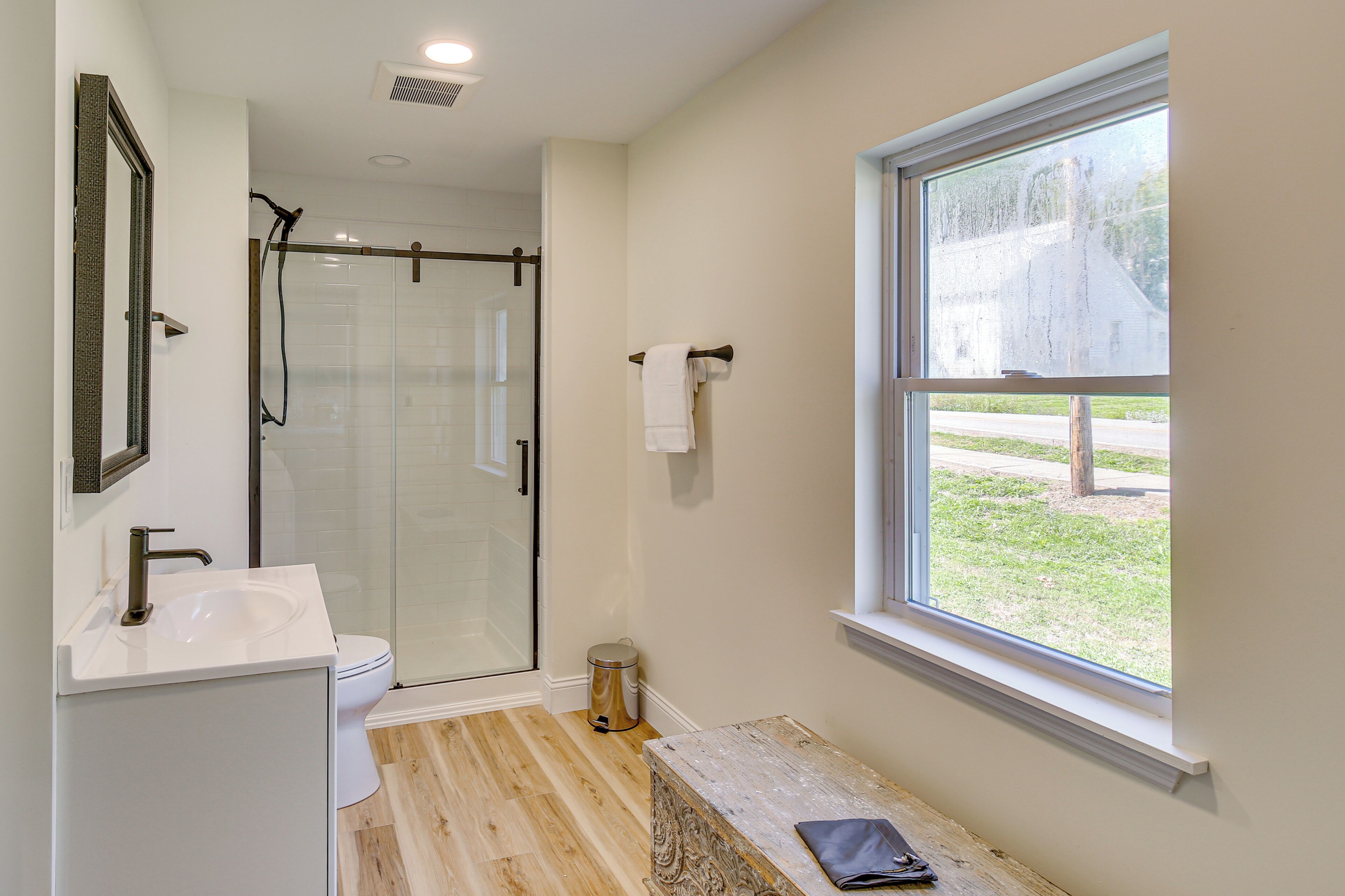 A bathroom with a glass shower enclosure, a sink, a toilet, and a window with a view of the outdoors.