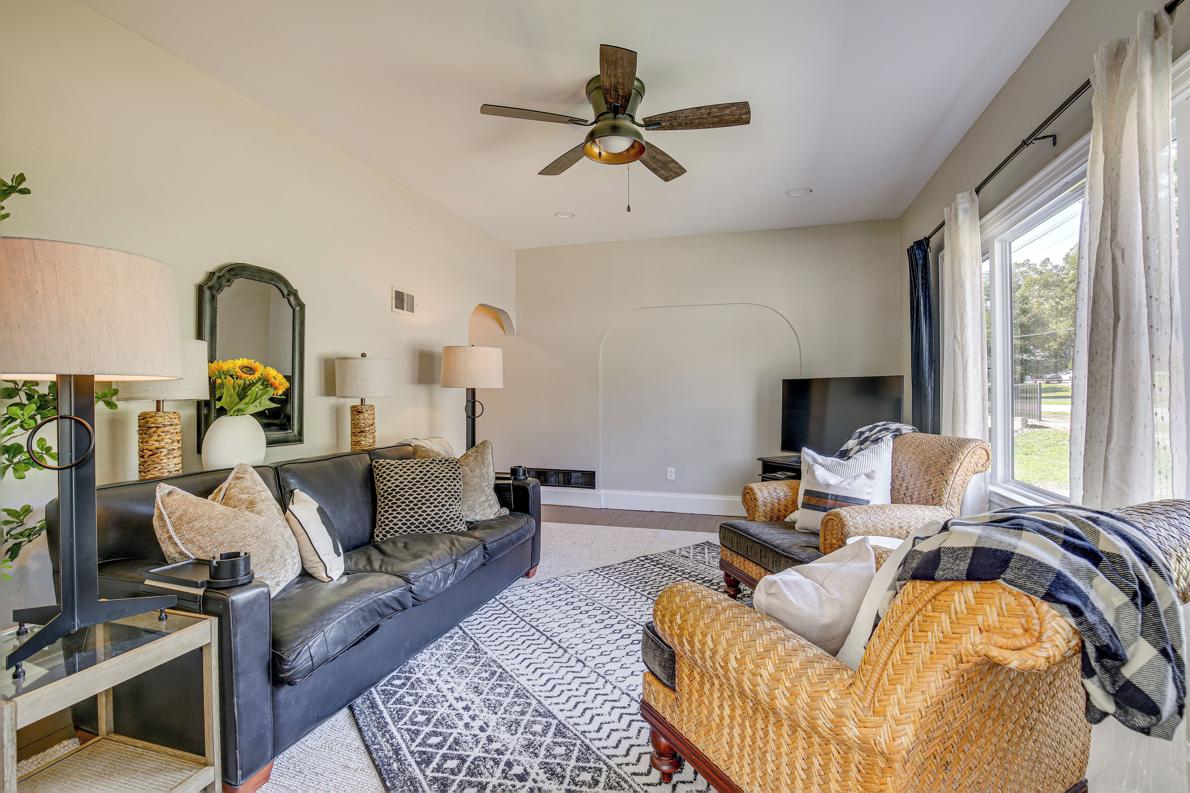 Un salon spacieux comprenant un grand canapé, un canapé plus petit, une table basse et un téléviseur. On y trouve également un ventilateur de plafond, une lampe et une fenêtre avec des rideaux.
