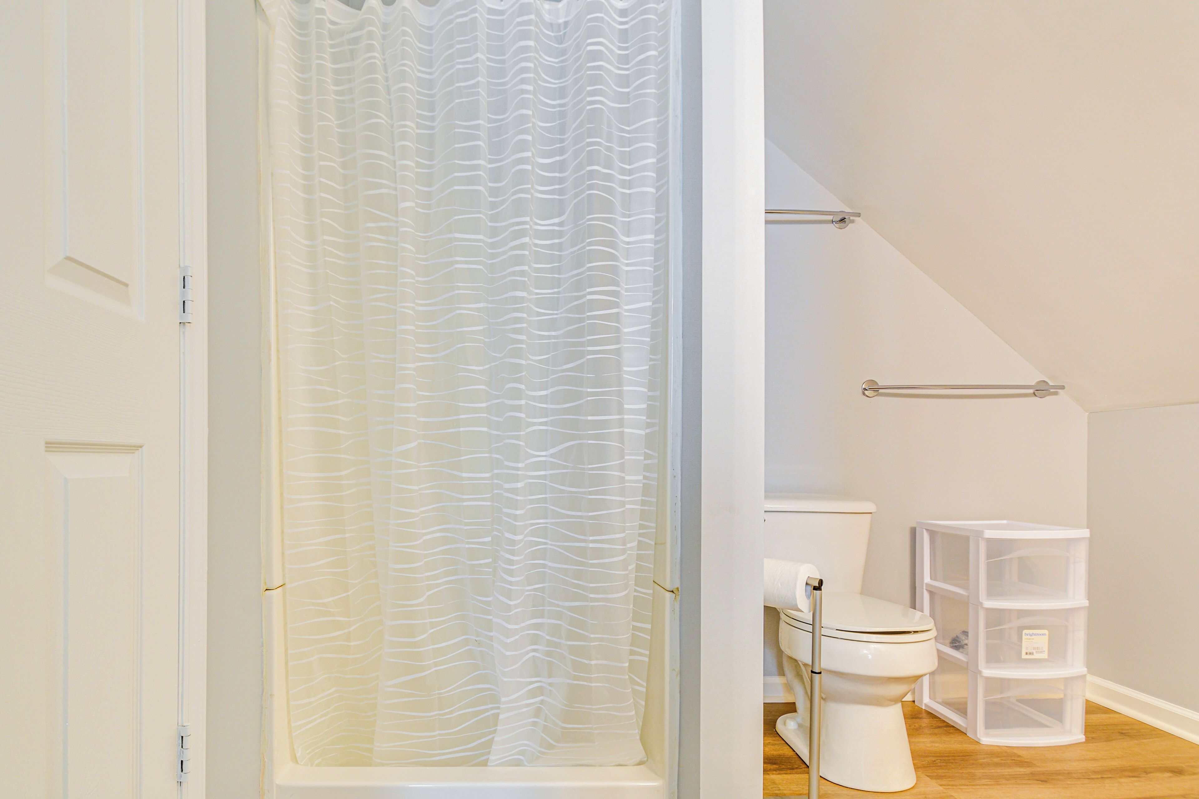 Et badeværelse med bruseforhæng, toilet og opbevaringsplads.