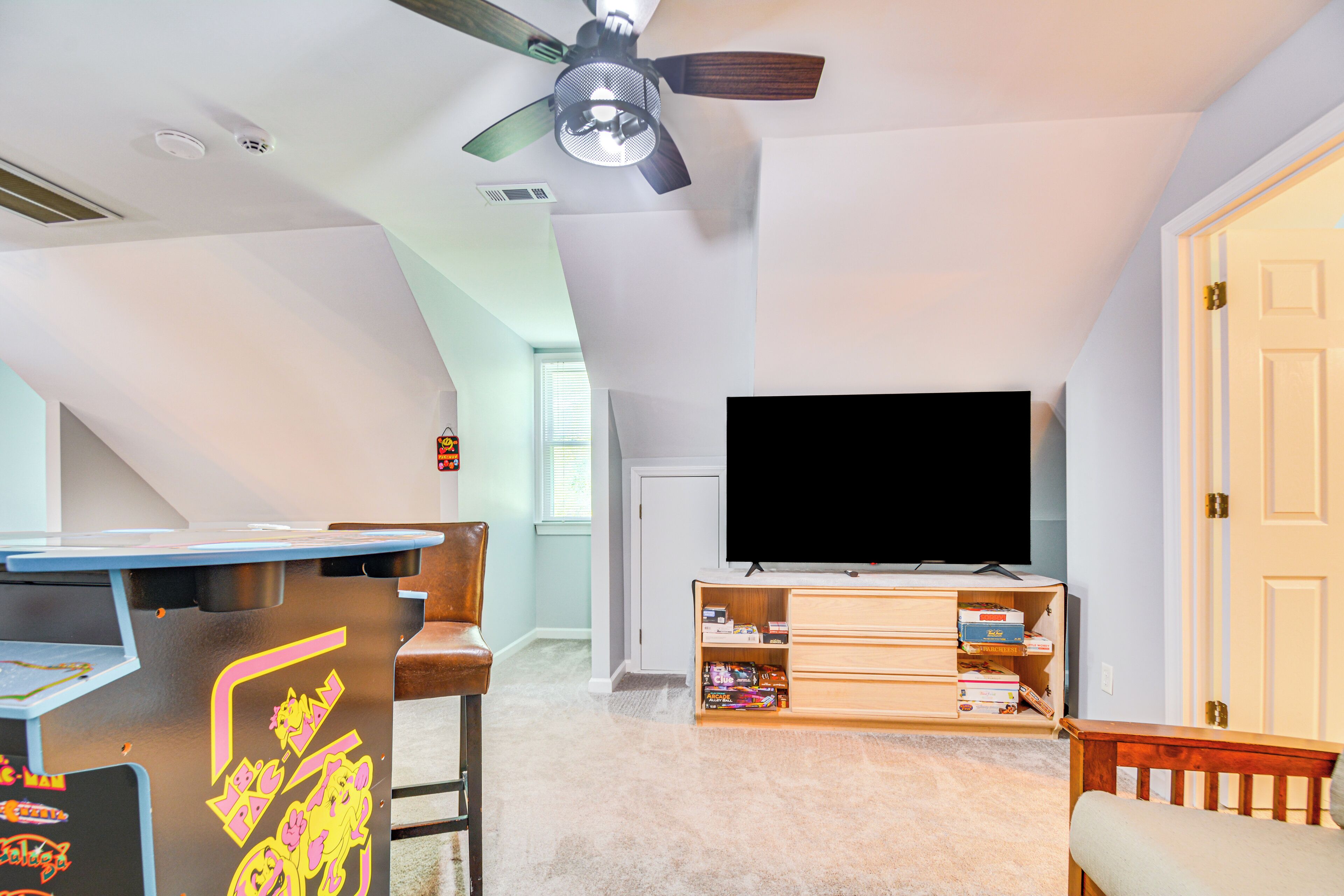 Quarto com ventoinha no teto, televisão de tela plana, móvel de entretenimento em madeira e área de bar com banquetas.