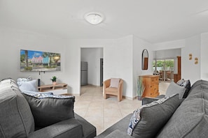 A modern living room with grey sofas, a coffee table, a TV mounted on the wall, and a painting of a colorful street scene. - Aruba Oasis: 3BR Home w/ Pvt Pool near Palm Beach (Noord)