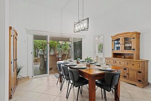 Ein Essbereich mit einem Holztisch, gedeckt für sechs Personen, umgeben von Stühlen, einem Schrank und einer Glastür zum Garten.