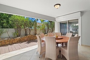 An outdoor dining area with wicker chairs and a round table, surrounded by a stone wall and greenery. - Aruba Oasis: 3BR Home w/ Pvt Pool near Palm Beach (Noord)