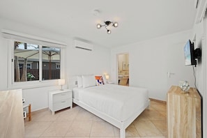 A bedroom with a bed, bedside tables, a TV, and a window. - Aruba Oasis: 3BR Home w/ Pvt Pool near Palm Beach (Noord)