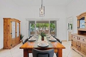 A dining area with a wooden table set for six, surrounded by chairs, with a view of greenery outside. - Aruba Oasis: 3BR Home w/ Pvt Pool near Palm Beach (Noord)