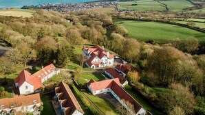 A rural area with houses, a large building with a red roof, and a view of the sea.