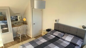 A bedroom with a bed, bedside table, lamp, chair, and a door leading to another room.