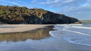 A beach with a rocky cliff, calm waves, and a clear sky. - Holiday Let Tresaith - Clos Y Hendy Lodge (Tresaith)
