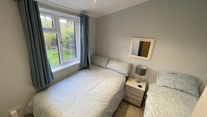 A bedroom with two beds, a window with curtains, a bedside table with a lamp, and a mirror on the wall. - Holiday Let Tresaith - Clos Y Hendy Lodge (Tresaith)