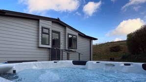 A hot tub with a house in the background. - Holiday Let Tresaith - Clos Y Hendy Lodge (Tresaith)