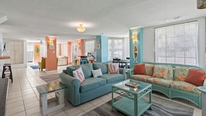 Un salon spacieux avec un canapé de couleur turquoise, une table basse en verre et un coin repas à l’arrière-plan.