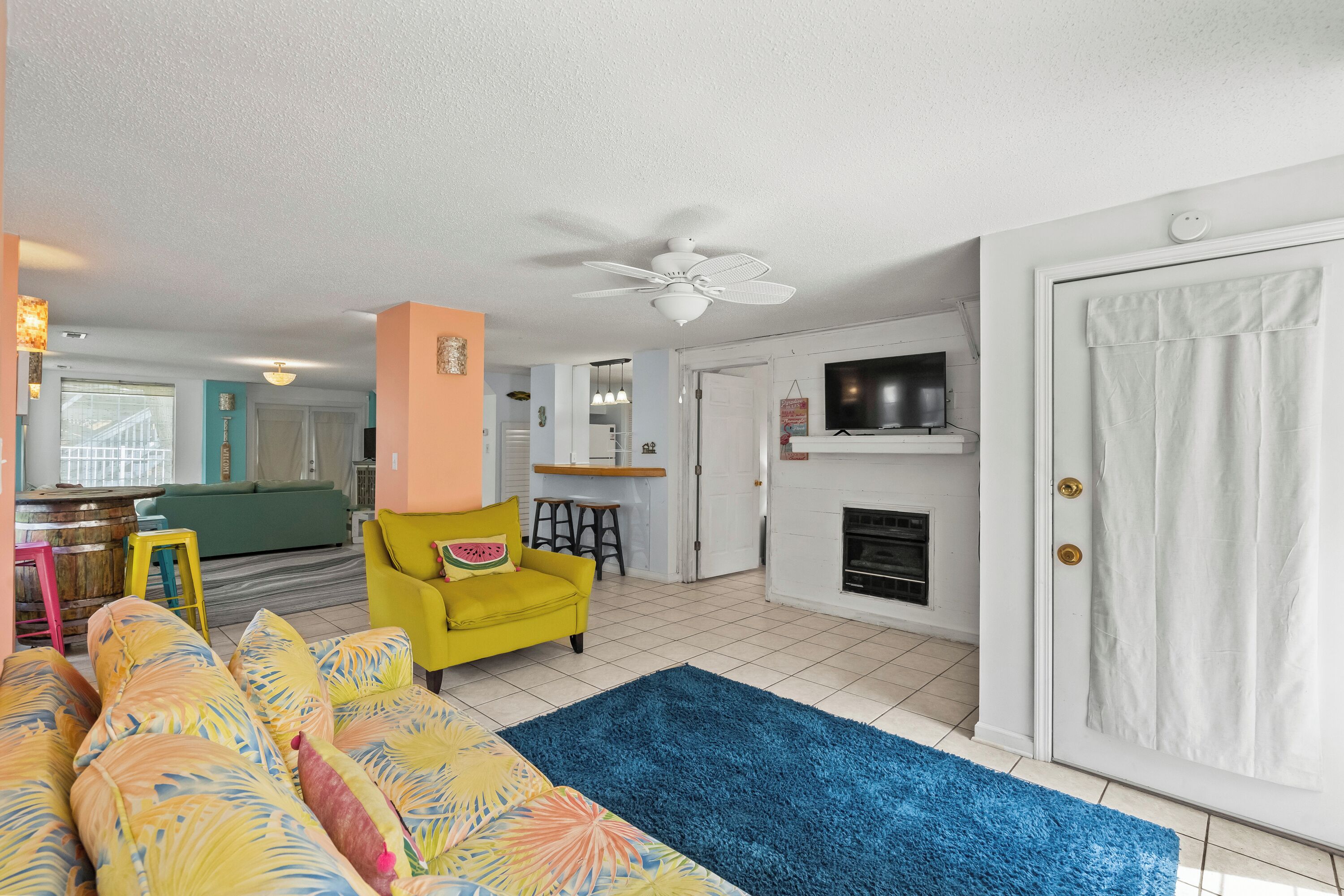 A living room with a sofa, a yellow armchair, a fireplace, and a ceiling fan.