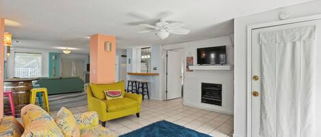 Una sala de estar con un sofá, un sillón amarillo, una chimenea y un ventilador de techo.