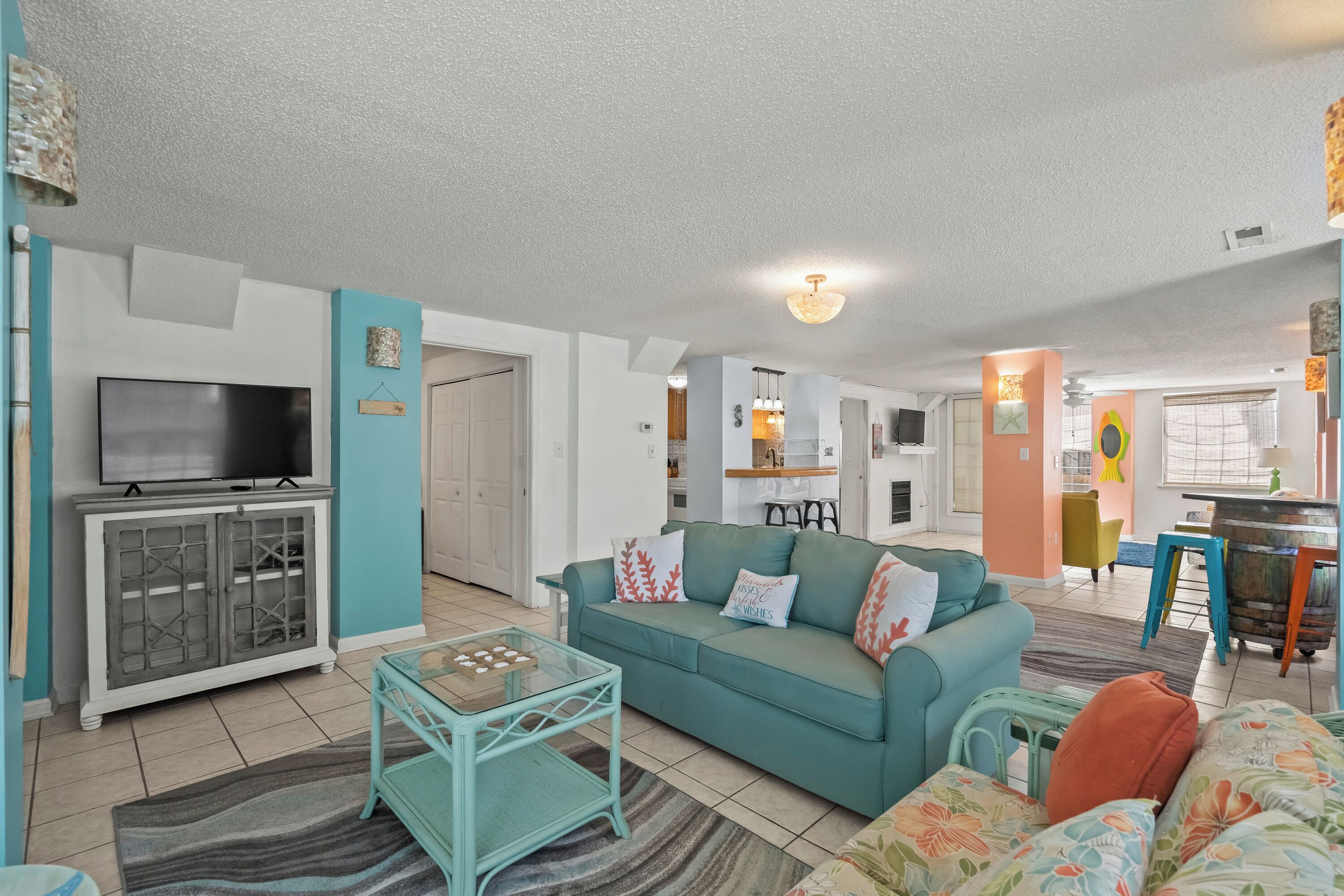 A living room with a teal sofa, a glass coffee table, and a flat-screen TV.