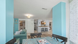 Un coin repas avec une table dressée pour quatre personnes, une cuisine en arrière-plan et un mur de couleur turquoise.