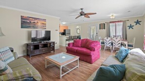A living room with a television, a pink sofa, and a glass coffee table. - Surfs Up - Coastal Escape (Surfside Beach)