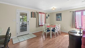 A dining area with a table and chairs, a door leading outside, and a window with curtains. - Surfs Up - Coastal Escape (Surfside Beach)