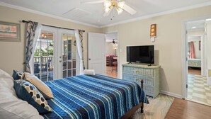 A bedroom with a bed, a television on a dresser, a ceiling fan, and a view of the outdoors through a door. - Surfs Up - Coastal Escape (Surfside Beach)