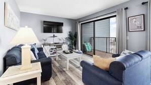 Un salon moderne avec un canapé, une table basse et un téléviseur. Il y a un balcon avec vue.