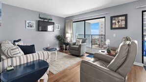 A modern living room with a sofa, armchair, and a TV mounted on the wall. - B512 at The Myrtle Beach Resort (Myrtle Beach)