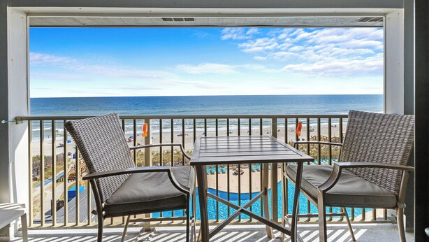 A balcony with two wicker chairs and a small table, overlooking a beach and a pool. - A504 at The Myrtle Beach Resort (Myrtle Beach)