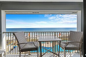 Un balcon avec deux fauteuils en osier et une petite table, donnant sur une plage et une piscine.