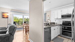 A modern kitchen with white cabinets, stainless steel appliances, and a large window overlooking a balcony.