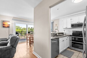 A modern kitchen with white cabinets, stainless steel appliances, and a large window overlooking a balcony.