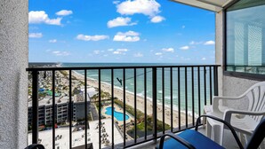 Ein Balkon mit Blick auf Strand und Meer, ausgestattet mit Pool, Liegestühlen und einer Essecke.