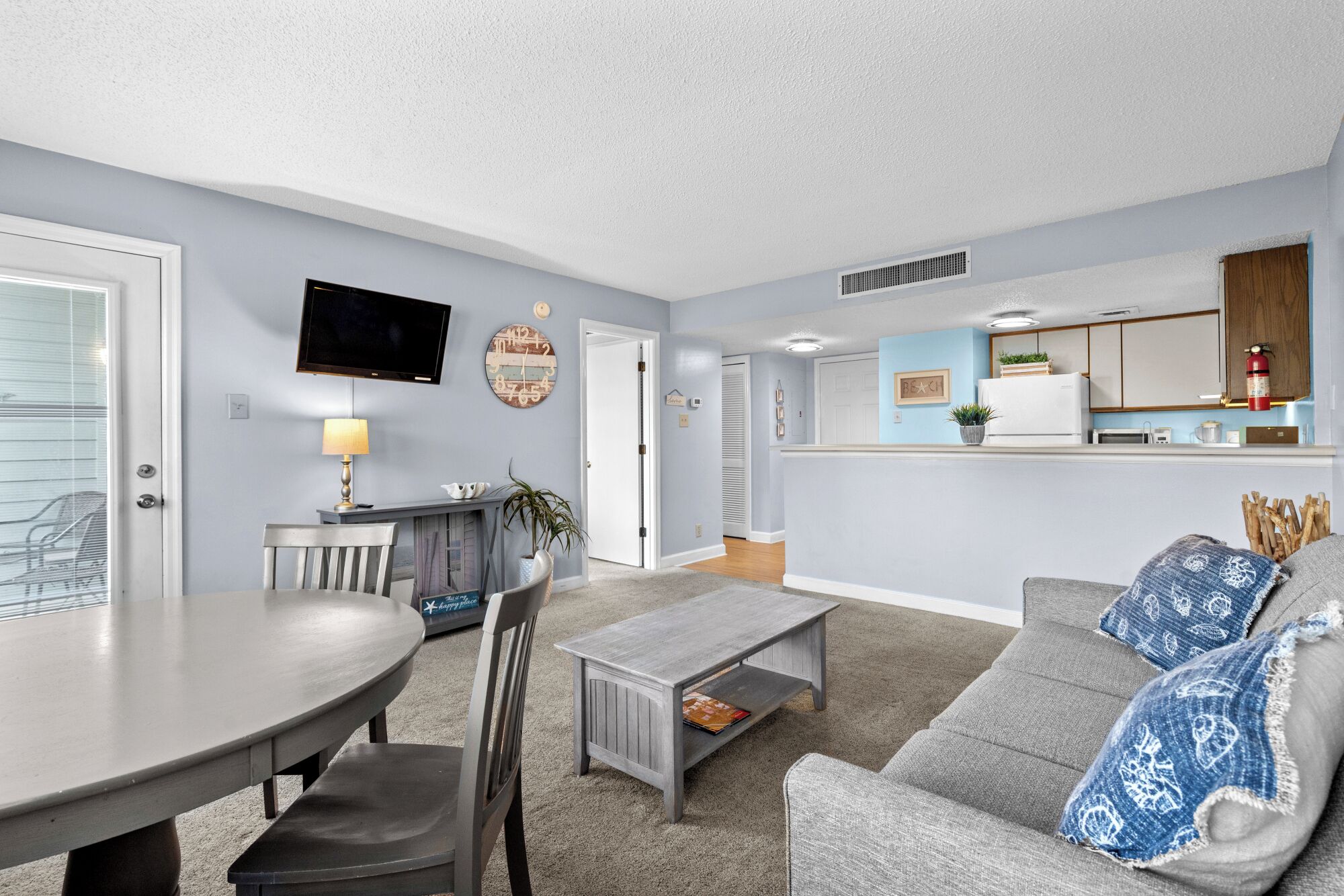 A living room with a dining table, a gray sofa, a coffee table, and a TV mounted on the wall.