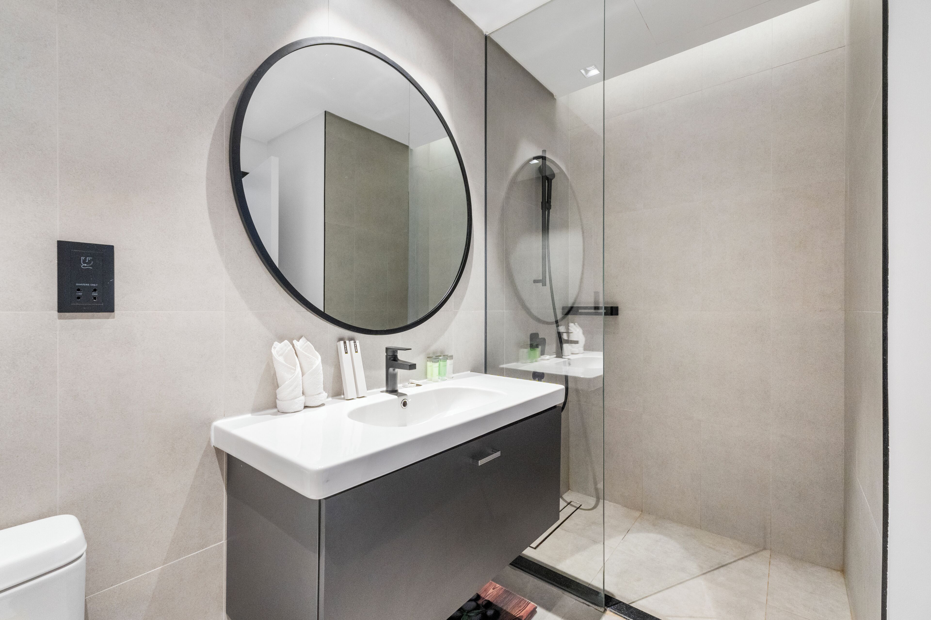 A modern bathroom with a round mirror, a white sink, and a glass-enclosed shower.