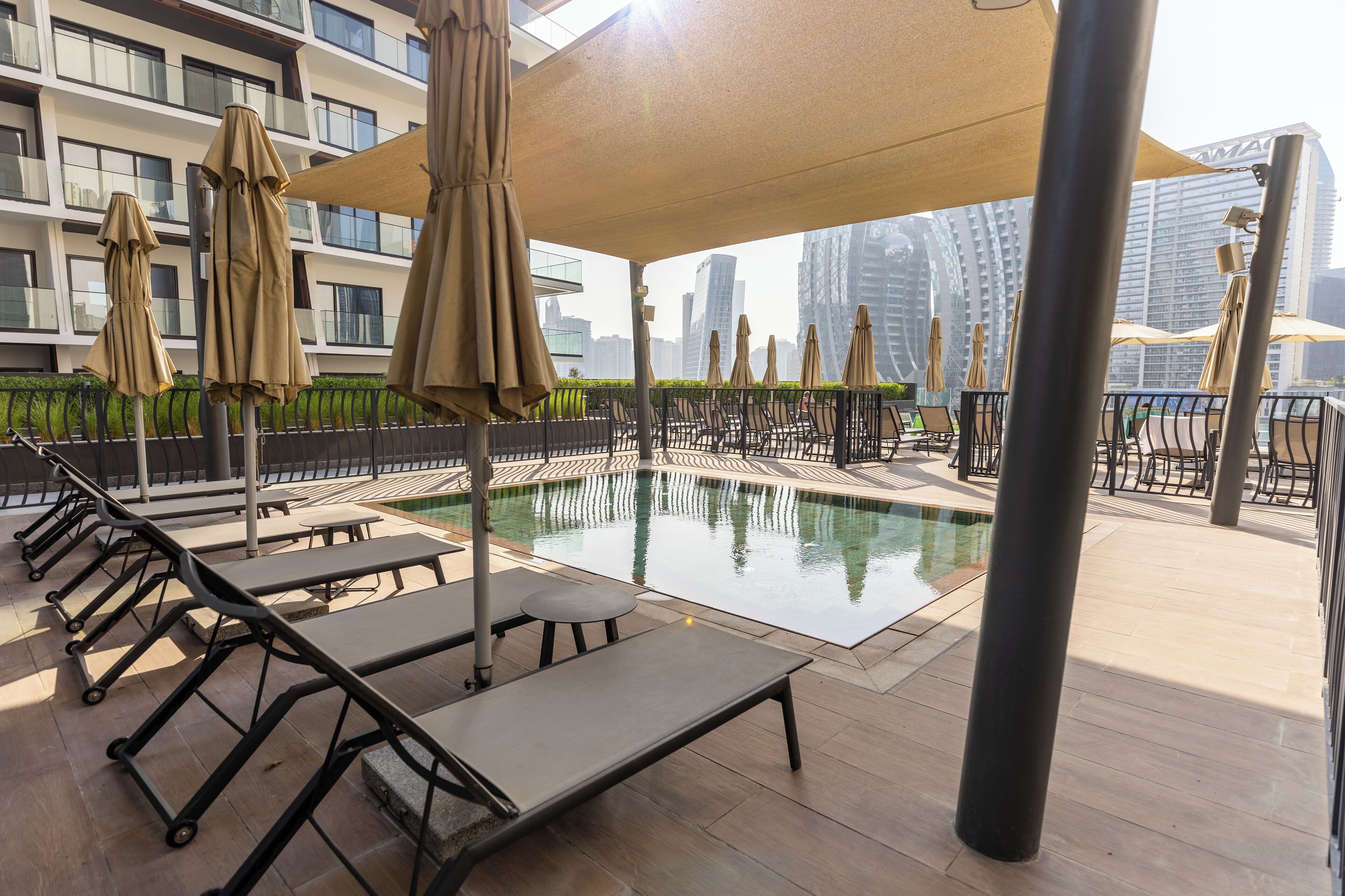 A rooftop pool area with lounge chairs and umbrellas, surrounded by a high-rise building.