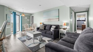 Een moderne woonkamer met een grijze bank, een salontafel, en een eethoek met stoelen.