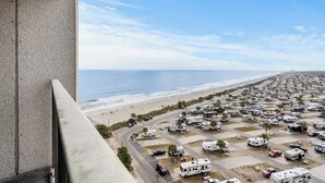 Une vue d’un terrain de camping pour véhicules récréatifs situé en bord de mer, avec des rangées de véhicules récréatifs stationnés le long de la côte, un ciel dégagé et l’océan en arrière-plan.