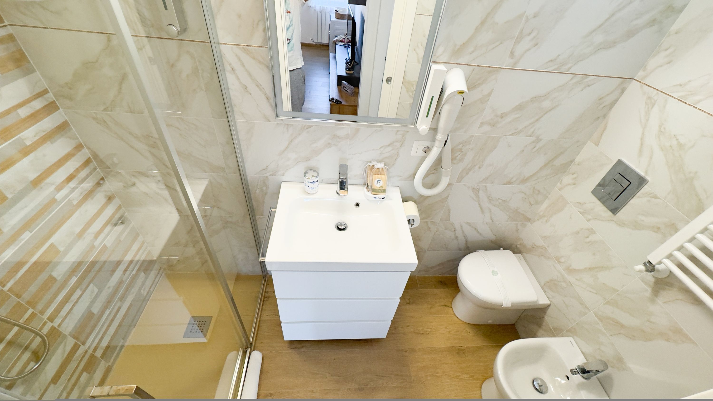 A bathroom with a white sink, toilet, and bidet, marble walls, and a glass shower enclosure.