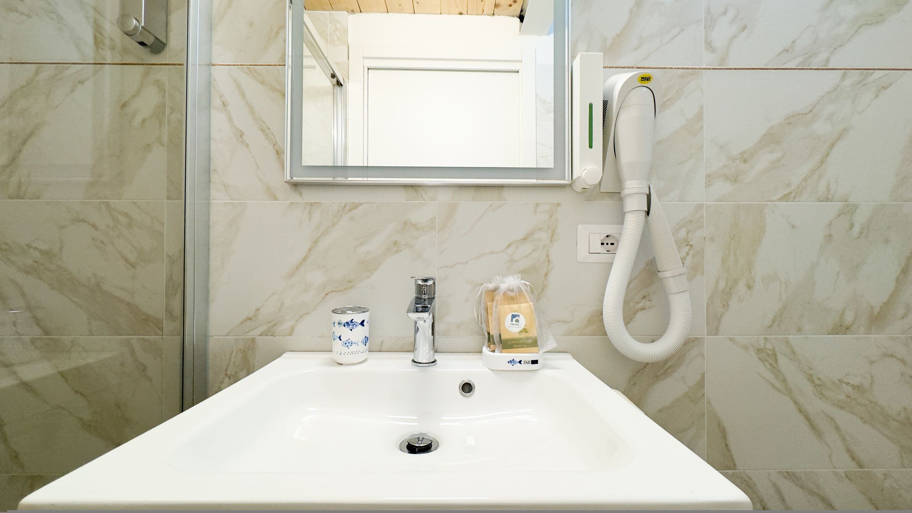 Een badkamer met een witte wastafel, een spiegel, een handdroger en een kleine zeepfles.