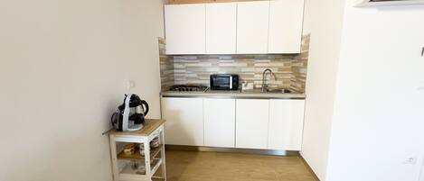 A compact kitchen with white cabinets, a microwave, a gas stove, and a small cart with cups.