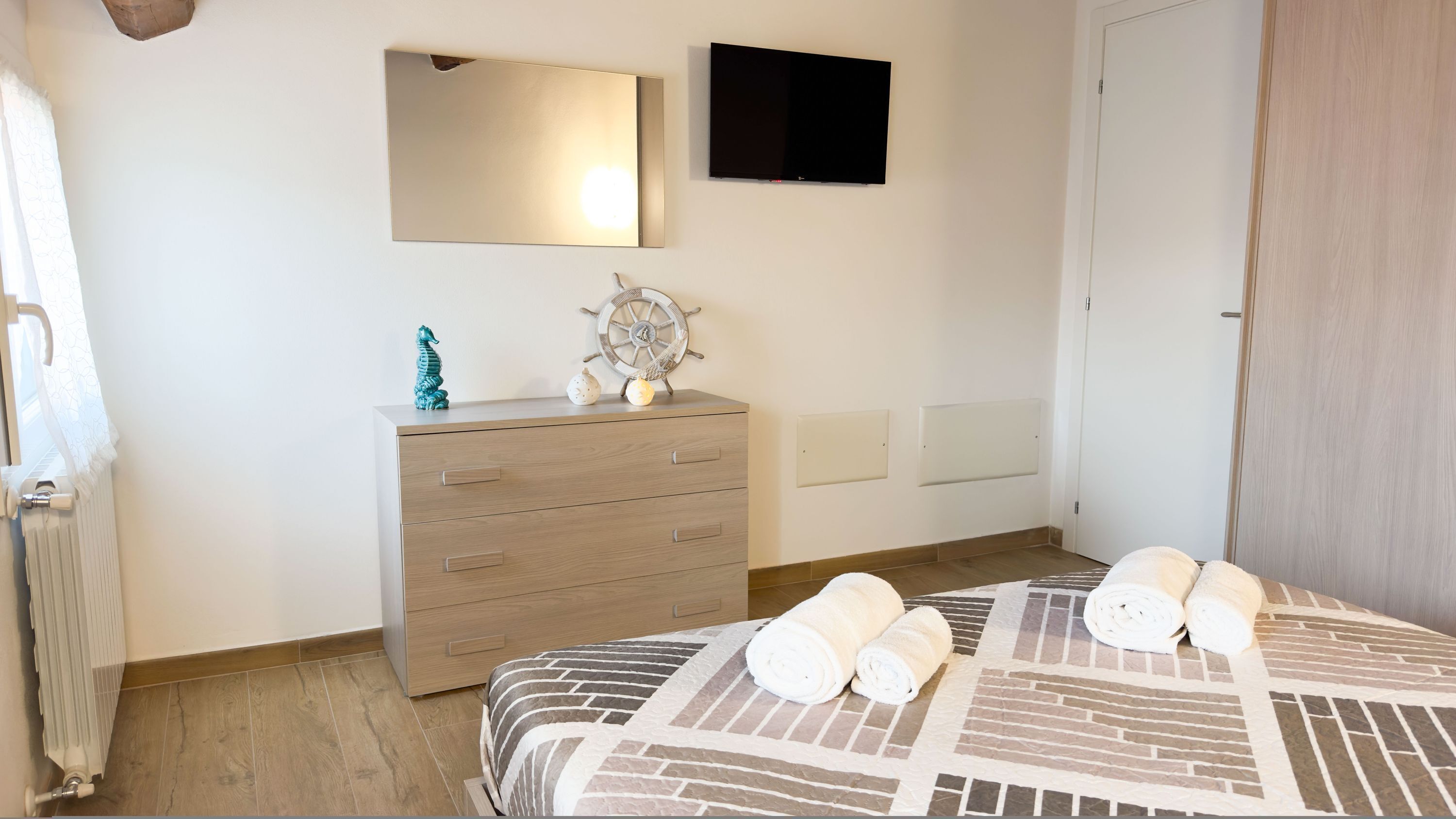 A bedroom with a bed, a dresser, a mirror, a TV, and a door.