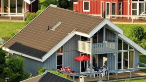 Una casa a due piani con un balcone, un patio con sedie e un ombrellone, e un fienile rosso sullo sfondo.