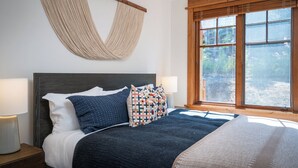 Un dormitorio con cama, dos lámparas de noche, un ventanal grande y un tapiz tejido en la pared.
