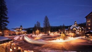 Una calle nevada al anochecer, con edificios iluminados y un cielo despejado.