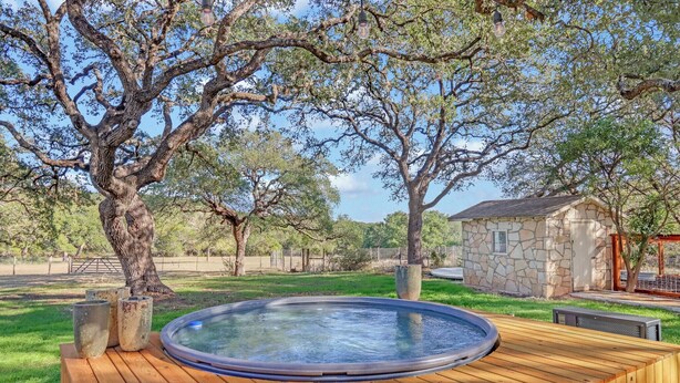 A wooden deck with a hot tub, surrounded by trees and a stone building. - Lawlis Lodge I Families, Star Gazing (Wimberley)