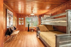 Une cabane aux murs et au plancher en bois, avec un lit superposé, un bureau et une chaise.