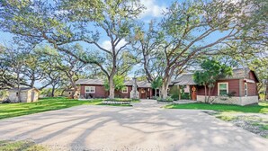 A residential property with a driveway leading to a brick house, surrounded by trees and a well-maintained lawn. - Lawlis Lodge I Families, Star Gazing (Wimberley)