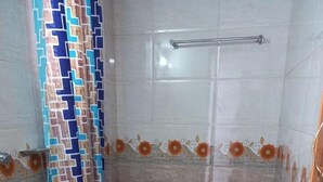 Ein kleines Badezimmer mit Toilette, Duschvorhang, Handtuchhalter und einem roten Eimer.