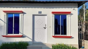 Ein kleines, eingeschossiges Gebäude mit weißer Fassade, einer rot gefassten Tür und zwei Fenstern mit roten Rahmen.