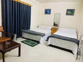 Quarto de hotel com duas camas, uma cadeira, uma mesinha, uma lixeira e duas fotos emolduradas na parede.